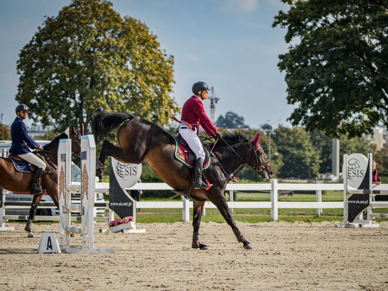 Two equestrians competing in an outdoor show jumping event, showcasing skill and agility.